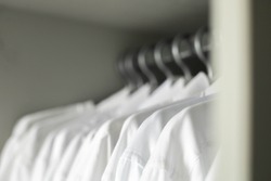 Many white collar clean male shirts on hangers cupboard business clothes storage organization closeup. Man wardrobe fabric textile formal fashion clothing professional monotone uniform garment attire