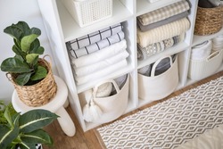 Neatly folded linen cupboard shelves storage at eco friendly straw basket placed closet organizer drawer divider. Stacks towels pillows plaids soft sheets bedding cabinet filling Nordic organization