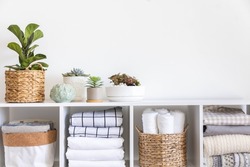Potted plants in ecology straw baskets on shelf of bed linens cupboard textile arrangement storage organization. Minimalism Scandi placed method neatly folded cotton fabric bedding material copy space