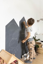 Cute baby boy drawing on black chalkboard use colorful chalks indoor at childish playroom kindergarten. Funny playful male kid creative art picture use crayon at home. Adorable baby happy childhood