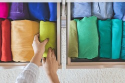 Women's hands take bright rainbow clothes from a wardrobe drawer. The concept of order and storage. Vertical storage method. Topview.