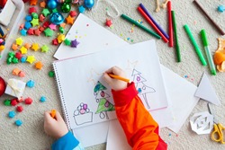 A boy draws a Christmas tree. Child's drawing Christmas. The child lies on the floor and draws in a notebook with white paper.