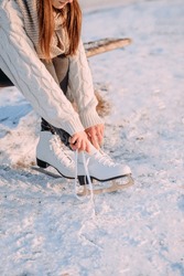 A young girl ties her skate laces before skating at the skating rink. White figure skating skates worn on a woman's feet. Side view. Active recreation in winter.