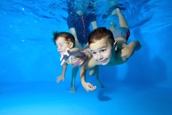 Two children, a small boy and a girl, are engaged in swimming in a children's pool. They play and dive under the water with their eyes open, and a female instructor helps them. Close up. Concept.