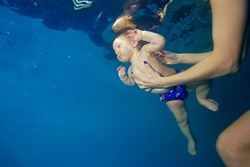 Mom coach teaches baby to swim underwater in the pool and maintains his hands. Portrait. Shooting under water. Bottom view. Landscape orientation