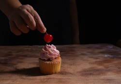     Putting a cherry on the pink cupcake on wooden table                             