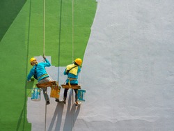 Two painters are painting the exterior of the building on a dangerous looking scaffolding hanging from a tall building with copy space.
