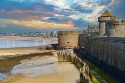 Skyline of the English Channel coast and the ancient fortress walls of the city of Saint-Malo during the ocean low tide in the evening against a dramatic sky. France                           