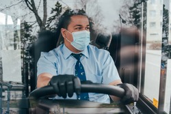 young hispanic man bus driver  in a protective mask and black gloves. prevent the spread of coronavirus. young hispanic bus driver wearing a protective mask and looks at road. quarantine. covid 19.