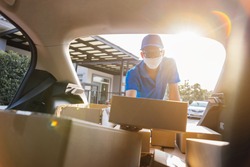 Asian Delivery man wearing mask picking up the package on front receiver shipping deliver cargo social distancing, Many parcel in trunk hatchback car while the virus is spreading at sunset.