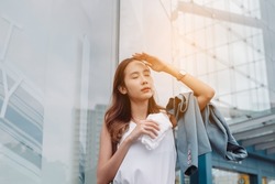 Asian businesswoman facial skin is damaged by UV attack from bright sun light in the modern city near office, Sun cream, sun block concept.