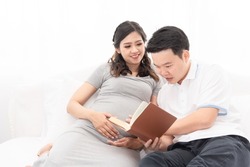 Asian new father spending time with his wife, excited dad expecting for newborn. Husband reading book to his wife preparing for new birth.