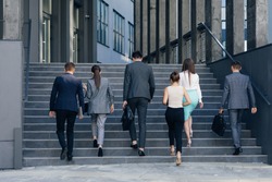 Rear view of Six Business People Walking up the Stairs. Men and women in formal suits going up stairs into office building. Partnership, communication business people concept.
