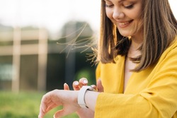 Smart watch. Smart watch on a woman's hand outdoor. Appealing young elegant woman touching a smartwatch. Caucasian woman use her wearable smart watch and smiling.