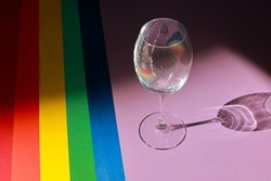 Top view of colored paper backgrounds laid out in the LGBT flag of pride with a glass. LGBT flag colors. Celebration concept.