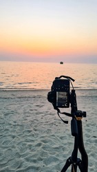 A photographer captures the beauty of the sunset on the coast of Kish Island, Iran. The photographer is silhouetted against the setting sun, creating a dramatic and evocative scene. 