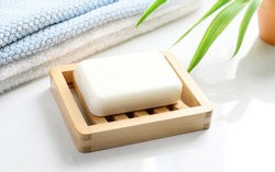 White Soap bar on wooden soap dish and cotton towels on white counter table in the bathroom.