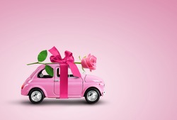Pink toy car delivering pink rose flower with ribbon and bowon pink background. Valentine day, flowers delivery, women day. Place for text.