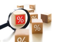 Choosing the best interest rate of a financial and mortgage loan. Wooden cube blocks with percentage symbol and magnifier on a white