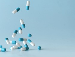 Falling blue medicine pill capsules on blue background. Antibiotics