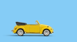 Model of yellow retro toy car cabriolet on solid blue background. Miniature car side view with copy space