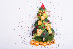 Christmas tree made of broccoli, mandarins, pomegranate seeds with glitter isolated on white background. Holiday decorations and meals.