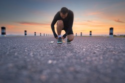 Running shoes - man sit down tying shoe laces. male sport fitness runner getting ready for jogging outdoors the time during sunrise on dam road exercise