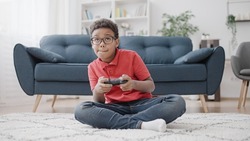 Concentrated African American boy having fun playing video game, controlling characters with joystick