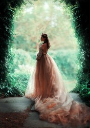 Beautiful Pregnant brunette woman in fairy long gold dress standing in green garden .Gorgeous young queen with perfect hair style and crown posing.Fantasy art work.