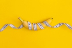 Measuring tape and banana on yellow background. Weight loss concept