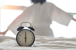 Woman on bed wake up stretching in bedroom with alarm clock at 6.00 a.m. morning. Biological Clock healthcare lifestyle concept