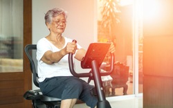 Active Asia senior old woman people training exercise on stationary bike for fit healthy at home gym.
