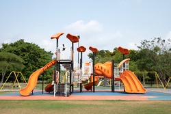 The outdoor playground in the daytime has a backdrop of green trees and blue skies.