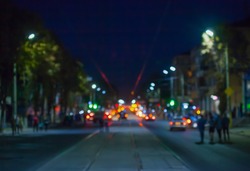 View of the street in the city at night blurred, where riding cars, trams, people walking, glow lights and vehicle headlights.