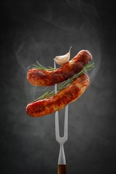 two fried hot thinking sausages on a meat fork with raspberry and garlic. grilled sausage, bbq concept