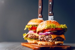 Two mouth-watering, delicious homemade burger used to chop beef. on the wooden table. The burgers are inserted knives.