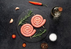 raw sausages in the form of a spiral on skewers on a stone background