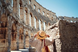 woman in hat stands and looking on Coliseum in Pula Croatia. travel concept.Young woman enjoy summer Italian vacation in Europe.