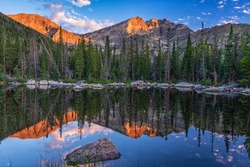 Ypsilon Mountain and Mount Chiquita are reflected in the calm water of Chipmunk Lake with the first light of golden hour in Rocky Mountain National Park, Colorado.