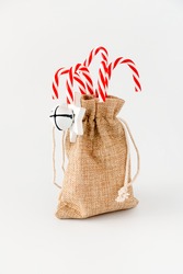 Red candy canes in jute sack with jingle bells and Christmas star isolated on white. Low angle view.
