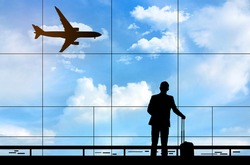 Silhouette of businessman standing at the terminal airport with airplane background, hand holding the luggage during waiting for flight boarding time, business and travelling concept.