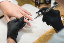 Closeup shot of a woman in a nail salon receiving a manicure by a beautician with airbrush. Woman getting nail manicure.