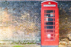 Traditional red telephone box on street of Hampstead Heath in London against a grungy brick wall