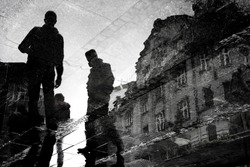 Blurry reflection silhouette of young men walking city streets  in black and white, low angle view with building , in the puddle