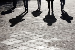 Legs and shadow of five young person approaching on city street pedestrian sidewalk