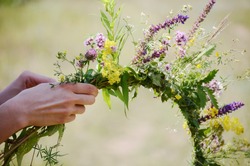 The girl makes a wreath at the head. The process of weaving a wreath with herbs and wild flowers. Summer. Spring