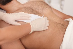 Cosmetologist doing waxing on torso of unrecognizable male client