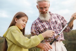 Cute young girl enjoying learning about fishing from her grandfather