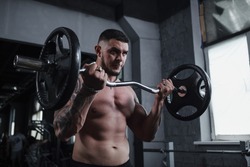Low angle shot of a handsome ripped tattooed male athlete working out with barbell, looking focused