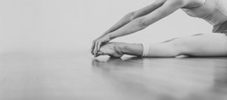 Black and white wallpaper faceless ballet dancer warming up in studio copy space room for text. No face dancing female feet legs stretching indoors toes professional arts. Modern contemporary art